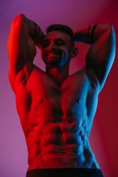 A muscular man with a beard is posing under the blue and red light. Stock Photos