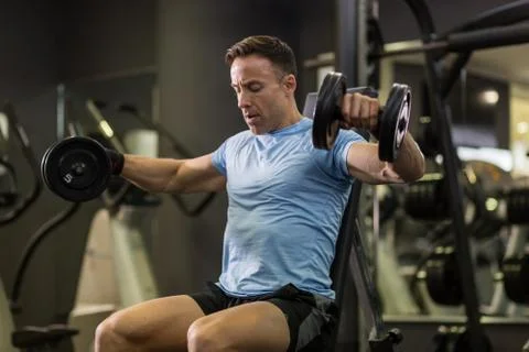 Muscular man doing exercise with dumbbell at the gym. Stock Photos