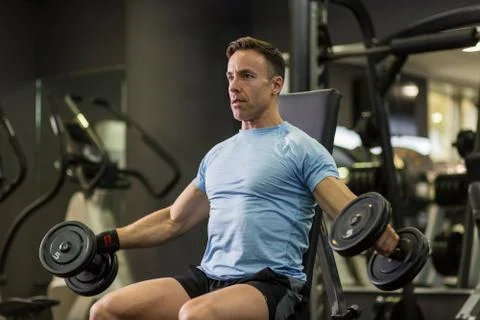 Muscular man doing exercise with dumbbell at the gym. Stock Photos