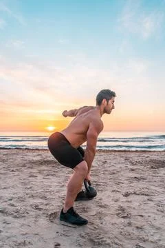 Muscular man doing functional training with kettlebell on the beach at 库存照片