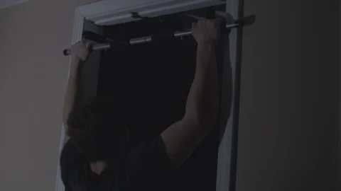 Muscular man doing pull-ups on a doorway bar at home in the dark. Stock Footage 86568877