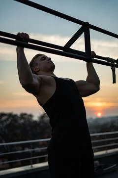 Muscular man doing pullups on sunset sky background. Concept of willpower Stock Photos