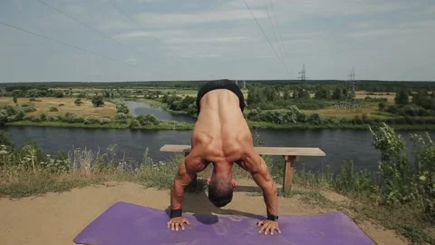 A muscular man doing push-ups on a rug by the river with his feet on a bench Stockbeeldmateriaal 138499337