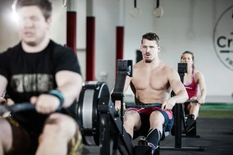 Muscular Man Exercising On Rowing Machine In Gym Stock Photos
