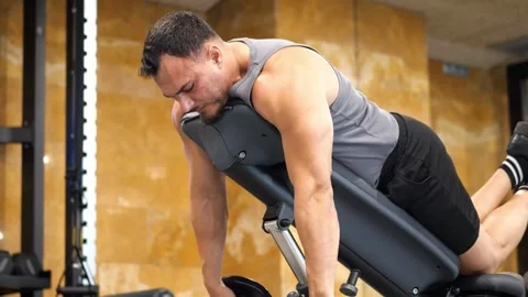 Muscular man lying on incline bench performing dumbbell rear delt flyes wit.. Vidéo 344052880