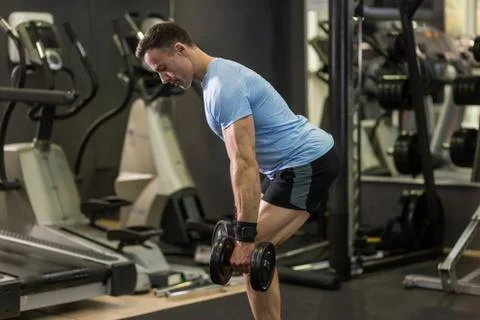 Muscular man pulling heavy dumbbell at the gym. Stock Photos