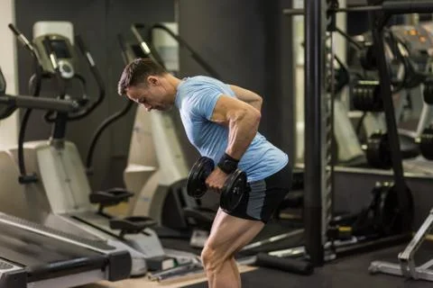 Muscular man pulling heavy dumbbell at the gym. Stock Photos