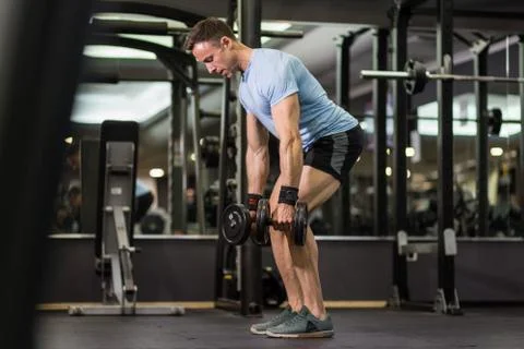 Muscular man pulling heavy dumbbell at the gym. Stock Photos