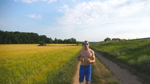 Muscular man running at country road. Young athletic guy jogging at rural trail Stock Footage