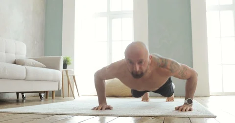 Muscular man in shorts is doing push-ups and dynamic exercises in plank at home. Stock Footage 129904079