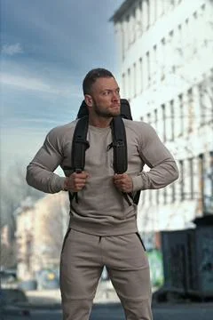 Muscular man in urban setting with backpack demonstrates strength and readiness Stock Photos