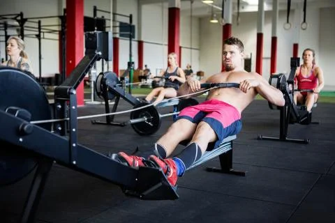 Muscular Man Using Rowing Machine In Gymnasium Foto stock