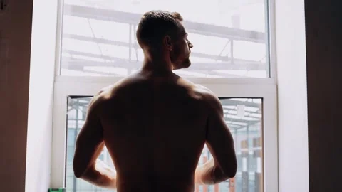 The muscular man's back against a window, the man looks out the window, the back Stock Footage 156509537