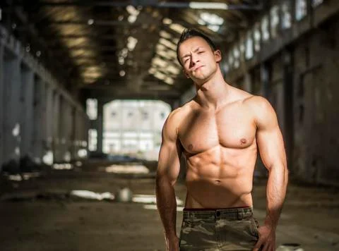 Muscular shirtless young man in abandoned warehouse standing Stock Photos