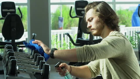 Muscular trainer spraying alcohol cleaning and disinfection dumbbell and equi Stock Footage 146318092