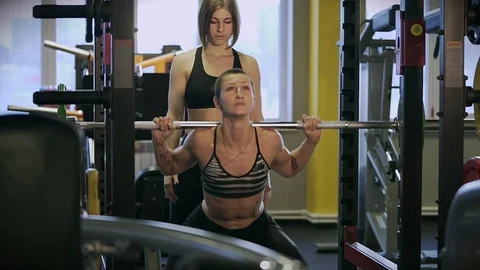 A muscular woman in an elastic suit crouches with a barbell in a sports club. Stock Footage