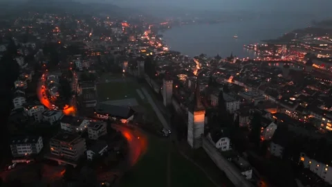 Musegg Wall and its nine towers aerial view at night overlooking glowing city in Видео 336751829