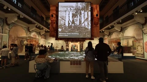 Museum visitors explore an interactive model display near a historical screen Stock Footage 339246752