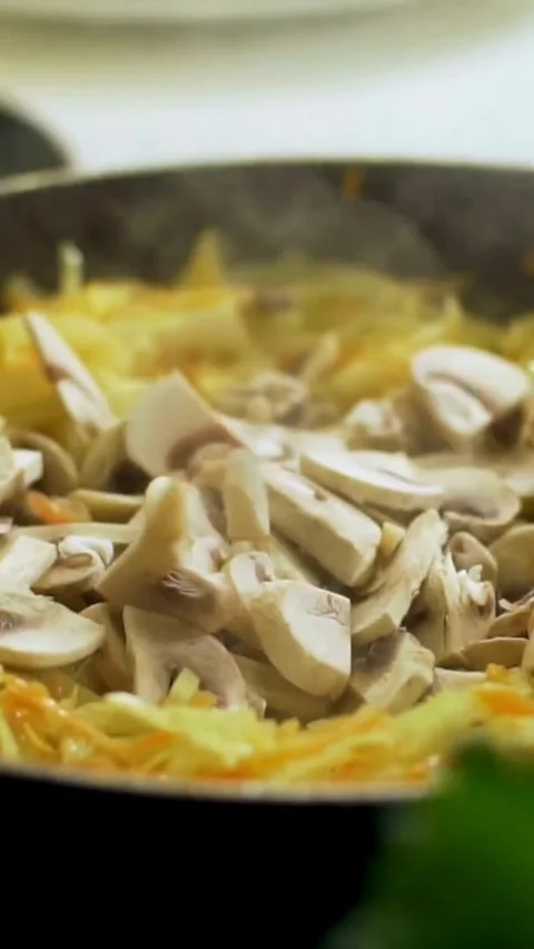 Mushrooms added to shredded cabbage in pan and stirred Stock Footage 334169858