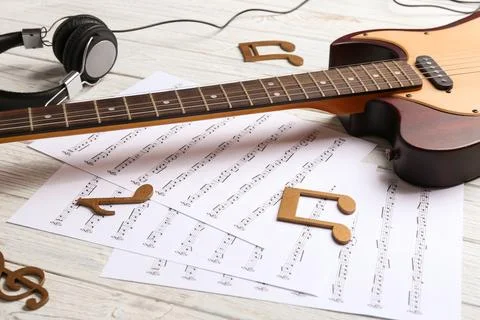 Music notes, headphones and guitar on white wooden table Stock Photos