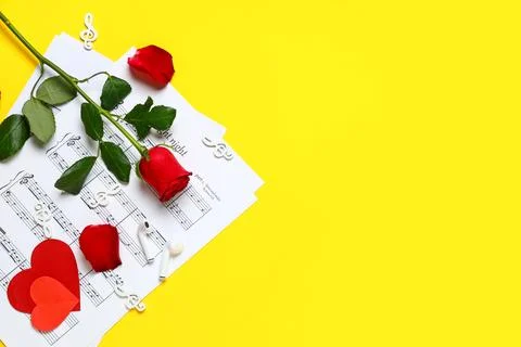 Music sheets with treble clefs, rose flower, earphones and paper hearts on ye Stock Photos