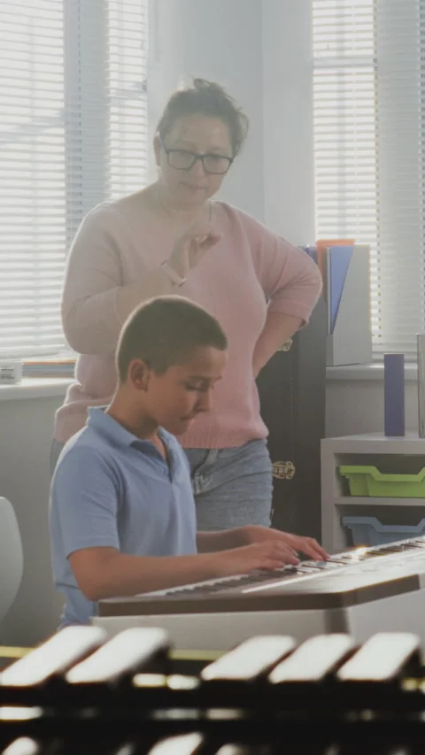 Music Teacher Guiding Primary School Boy to Play Piano in Music Class Stock Footage 317543278