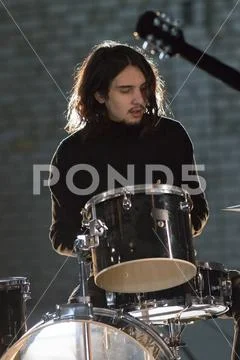 A musician man with long hair sitting by the drum-kit Stock Photos