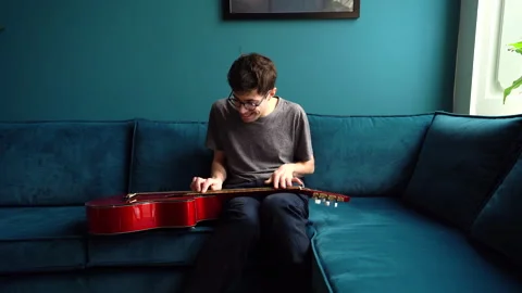 Musician Plucking Guitar Strings on Sofa Stock Footage 274231699