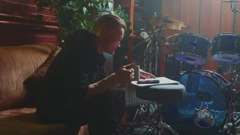 Musician reflects while sitting on a couch near a drum set Stock Footage 307118267