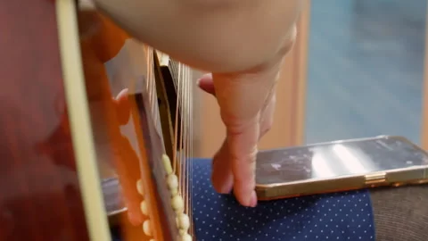 Musician using a tuner app on smartphone while playing acoustic guitar Video stock 301275053