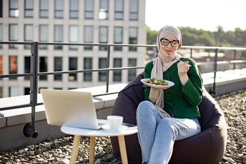 Muslim female dining while working remotely on roof terrace Stock Photos