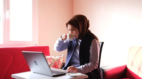 Muslim girl drinking coffee while working with laptop at home. Vídeo Stock 153499741