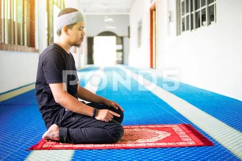 Muslim man praying, with one finger up on praying mat inside a mosque Stock Photos