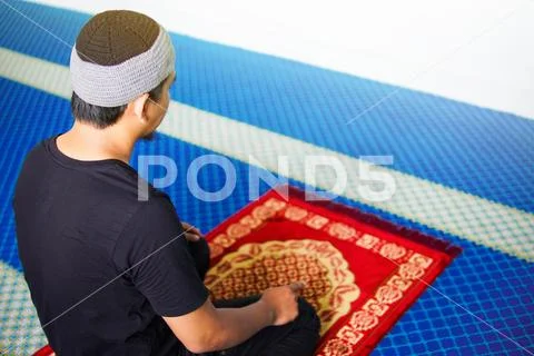 Muslim man praying, with one finger up on praying mat inside a mosque Stock Photos