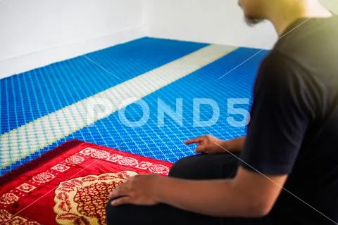 Muslim man praying, with one finger up on praying mat inside a mosque Stock Photos