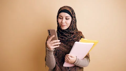 Muslim student using smartphone while holding notebooks Stock Footage 339037731