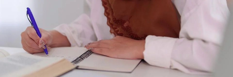 Muslim student writing notes in notebook studying at desk Islamic education.. Stock Photos