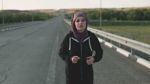 A Muslim woman with an open face does sports running on the side of an empty Stock Footage 133528448
