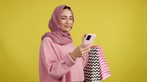 Muslim woman using the mobile while holing shopping bags Stock Footage 236808966