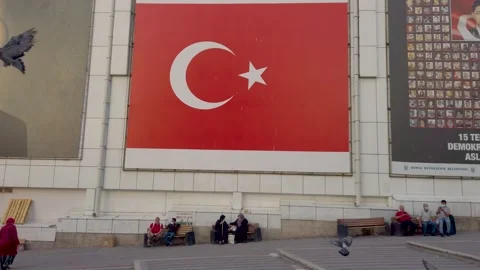 Muslims sitting under a Turkish flag in a square with pigeons Stock Footage 159182739