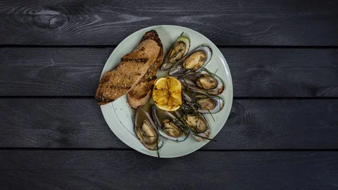 Mussels and bread toasts rotating on a plate. Is at a black wooden background Video stock 129186958