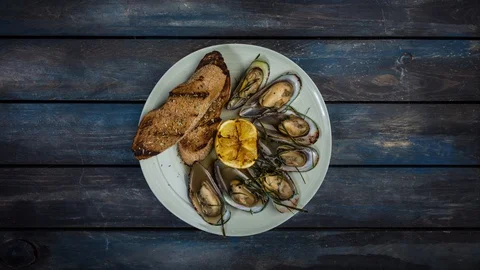 Mussels and bread toasts rotating on a plate. Is at a colored wooden background Video stock 129187039