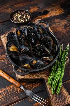 Mussels cooked with white wine sauce in a pan with herbs. Dark wooden background Stock Photos