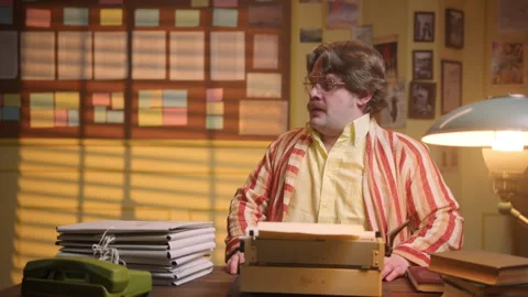 Mustachioed man types a text on a typewriter and a girl brings him a new stack Stock Footage 289569574