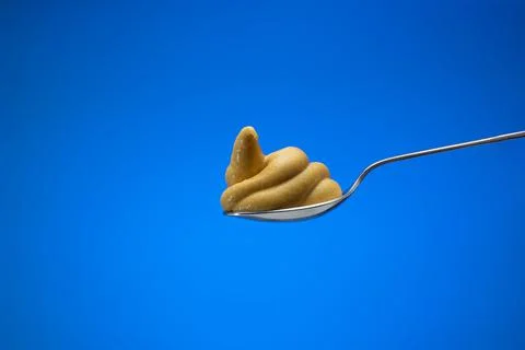Mustard paste on a small silver spoon Close up studio shot, isolated on blue  Fotos de archivo