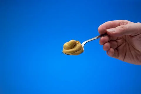 Mustard paste on a small silver spoon held in hand by man. Close up studio sh Fotos de archivo