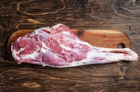 Mutton meat. Raw whole lamb leg thigh on butcher board. Wooden background. .. Stock Photos