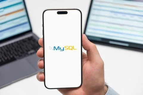 My SQL logo on the screen of smartphone in mans hand on the workplace background Stock Photos