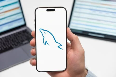 My SQL logo on the screen of smartphone in mans hand on the workplace background Foto stock