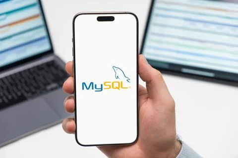 My SQL logo on the screen of smartphone in mans hand on the workplace background Foto stock
